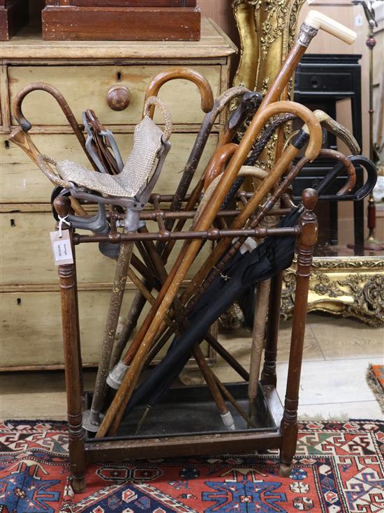 A stained beech umbrella stand, on turned supports with metal tray, together with a collection of walking sticks W.1ft 9in.